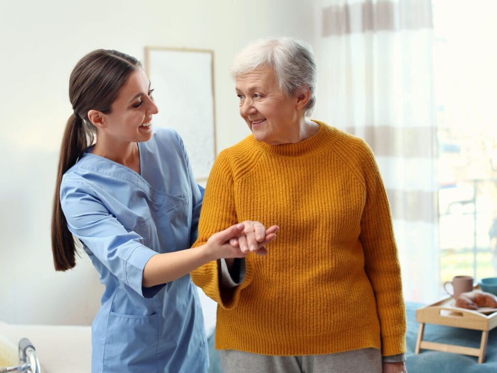 A live-in carer holds the hand of an older adult to guide her and support her to mobilise safely. Both are happy and making eye contact with each other that shows trust has been built between them.